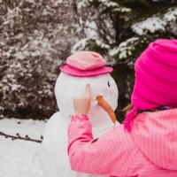 girl dressed in winter clothes makes a snowman in the backyard of their house in winter - garden decoration stock pictures, royalty-free photos & images