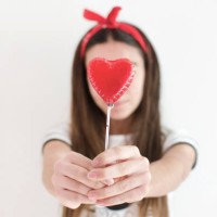 girl holding a heart shaped lollipop in front of her face - junk food stock-fotos und bilder