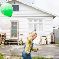 girl runs past the front of a bungalow holding colourful balloons - garden decoration stock pictures, royalty-free photos & images