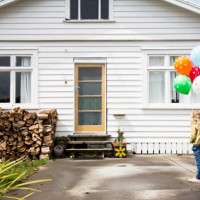 girl stands in front of a bungalow holding colourful balloons - garden decoration stock pictures, royalty-free photos & images