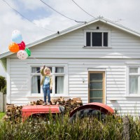 girl stands on a tractor holding colourful balloons in front of a bungalow - garden decoration stock pictures, royalty-free photos & images
