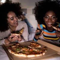 girlfriends lying down on bed and eating pizza - junk food stock pictures, royalty-free photos & images