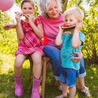 grandmother watching two children eating watermelons in garden - garden decoration stock pictures, royalty-free photos & images