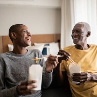 grandson and grandfather talking and eating take out food at home - junk food stock pictures, royalty-free photos & images