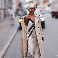 Grece Ghanem is seen wearing large gold hoop earrings; oval sunglasses with a tortoiseshell frame from Prada; a beige trench coat; underneath a...