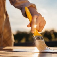 gros plan pinceau jaune tenu par une femme, table de peinture avec un rayon de soleil en vernis frais entre les doigts - garden decoration photos et images de collection