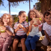 group of happy children sitting eating sandwiches in the garden - food stock pictures, royalty-free photos & images