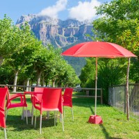 group of red chairs, tables and a parasol of a camping pub on green grass in torla - spain with the mountains of national park of ordesa at the background. horizontal photo. - garden decoration stock pictures, royalty-free ph