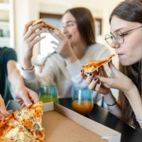 group of three teenagers eating pizza in a living room - junk food stock pictures, royalty-free photos & images