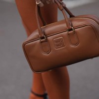 Guest holds a brown leather rectangle shaped bag from Miu Miu , outside Miu Miu, during the Womenswear Spring/Summer 2024 as part of Paris Fashion...