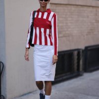 Guest is seen outside Brandon Maxwell show wearing blue sunnies, silver hoop earrings, white and red striped shirt, white midi cargo skirt and blue...