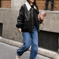 Guest is seen wearing a black and faux fur collar bomber jacket, blue jeans and white and black shoes with tan bag outside the Lacoste show during...