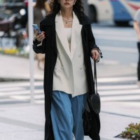 Guest is seen wearing a black trench coat, beige jacket, jeans, ALAÏA handbag, green shoes during Rakuten Tokyo Fashion Week A/W 2025 on March 22,...