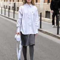 Guest is seen wearing a Lacoste button shirt, gray skirt, gray leggings, black shoes and white bag outside the Lacoste show during Womenswear...