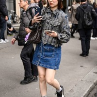 Guest is seen wearing a Sacai jacket, denim skirt, black sneakers and gray beanie outside the Sacai show during Womenswear Spring/Summer 2025 as part...