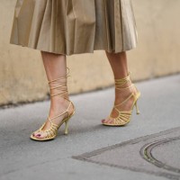 Guest wears a beige pleated / accordion midi skirt from Miu Miu, pale yellow shiny leather strappy heels sandals , outside Victoria Beckham, during...