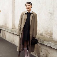 Guest wears a black dress, long white socks, black loafers, a brown trench coat, a black bag, and a metal Prada hair clip outside Prada during the...