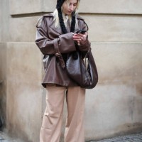 Guest wears a black hat with braids, a brown oversized leather jacket , a bag, beige flared pants, black and white shoes with crocodile patterns,...