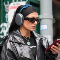 Guest wears a black headband, Apple airpods max, black sunglasses, a black and white t-shirt, a black leather jacket, outside La Pointe , during New...