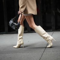 Guest wears a black leather bag, white pointed knee-high boots with high heels and crocodile pattern, outside Jason Wu, during New York Fashion Week,...