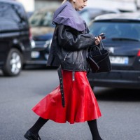 Guest wears a black leather jacket, a red leather midi skirt, tights, black leather shoes, a black leather bag, outside Undercover, during the...