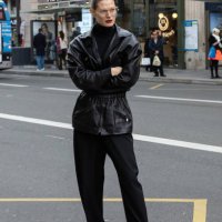 Guest wears a black leather jacket, black turtleneck, wide-leg black trousers, red pointed-toe heels, and clear-framed glasses outside Magda Butrym...