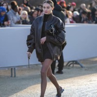 Guest wears a black leather oversize bomber jacket, a turtleneck black ribbed wool mini skirt, tights, leather shoes, outside Dior, during the...