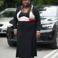 Guest wears a black ribbed long sleeves long dress with pale pink / red / blue print pattern tank-top, green shiny leather pointed heels shoes mules...