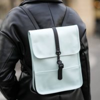 Guest wears a black shiny leather puffy / belted coat, a black and blue leather back pack bag, outside The Row, during Paris Fashion Week -...