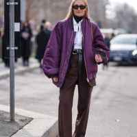 Guest wears a black turtleneck pullover, a white shirt, a purple bomber jacket, a black leather belt, brown pants, sunglasses, white sneakers shoes,...