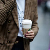 Guest wears a brown jacket, holds a Starbucks coffee cup, during London Fashion Week Fall Winter 2020 on February 16, 2020 in London, England.