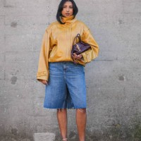 Guest wears a brown shiny leather jacket with puff sleeves, a burgundy leather bag, blue ripped denim / jeans shorts / jorts, kitten heels shoes,...