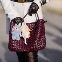 Guest wears a burgundy bordeaux woven Bottega Veneta Andiamo leather bag, light blue Labubu bag charm, cream Labubu bag charm, outside Elie Saab,...