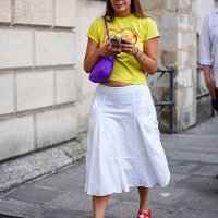 Guest wears a camouflage-patterned baseball cap and a bright yellow cropped T-shirt with a graphic print in red. A purple shoulder bag with a curved...