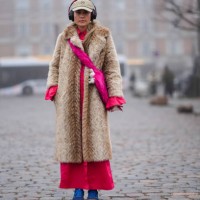 Guest wears a cap, a brown fluffy faux fur long coat, a pink dress, blue sneakers, headphones, outside Rolf Ekroth, during the Copenhagen Fashion...