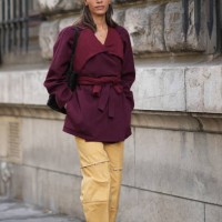 Guest wears a cap hat, a purple / burgundy wool coat, yellow trousers, mesh black shoes, outside Hermes, during the Womenswear Spring/Summer 2024 as...