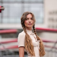Guest wears a cream-colored, short-sleeved top featuring a high collar and a keyhole cutout with a bow detail at the front. Hair is styled in two...