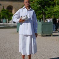 Guest wears a crisp white button-up shirt with a classic collar and long sleeves. The shirt is paired with a matching white midi skirt. Accessories...