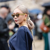 Guest wears a dark blue satin ensemble featuring a draped top with a cutout detail at the waist and long sleeves. The outfit includes a matching...