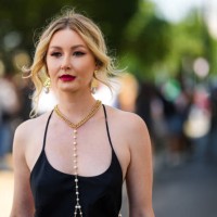 Guest wears a gold with pearl pendant earrings, a gold necklace with long pearls pendant details, a black tank-top long summer dress, outside the...