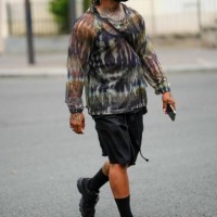 Guest wears a green headphones, a black mesh / fishnet tank-top, a brown / khaki / black tie and dye print pattern long sleeves t-shirt, black suit...