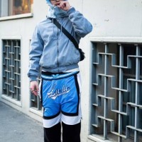 Guest wears a grey baclava, grey sunglasses, a black crossbody bag, a grey jacket, black, white and light blue wide leg trousers and black shoes...