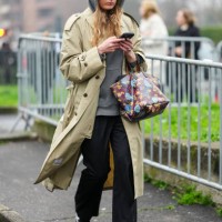 Guest wears a grey hoodie, a cream coat, black pants, burgundy leather bag with floral details, black leather sneakers shoes, outside Gucci, during...