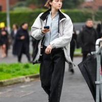 Guest wears a grey pullover, a white and black jacket, black wide-leg denim jeans / pants, black sneakers shoes, outside Gucci, during the Milan...