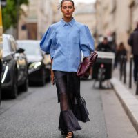 Guest wears a light blue oversized shirt, a black transparent long skirt, a burgundy leather bag, black leather shoes, outside Sacai, during...