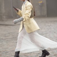 Guest wears a long white maxi skirt, grey hand warmers, Dior bag, and pale yellow jacket outside Rolf Ekroth during the Copenhagen Fashion Week AW24...