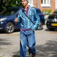Guest wears a pale gray felt wool beret, black sunglasses, a purple zipper high neck polo shirt, a blue and black shiny leather snake print pattern...
