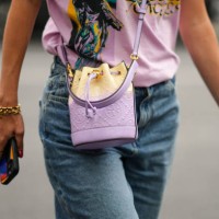 Guest wears a pale purple with green and yellow print pattern t-shirt, a pale purple shiny leather embossed monogram pattern crossbody bag from Tory...