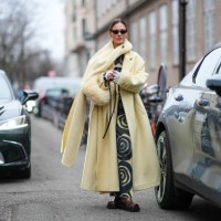 Guest wears a pastel pale yellow full look, an oversized scarf, sunglasses, a black and yellow dress with printed geometric patterns, brown leather...