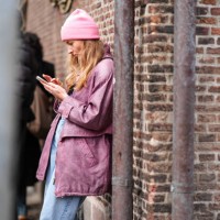 Guest wears a pink wool beanie hat, a purple leather jacket , blue denim jeans pants , outside The Garment, during the Copenhagen Fashion Week AW24...